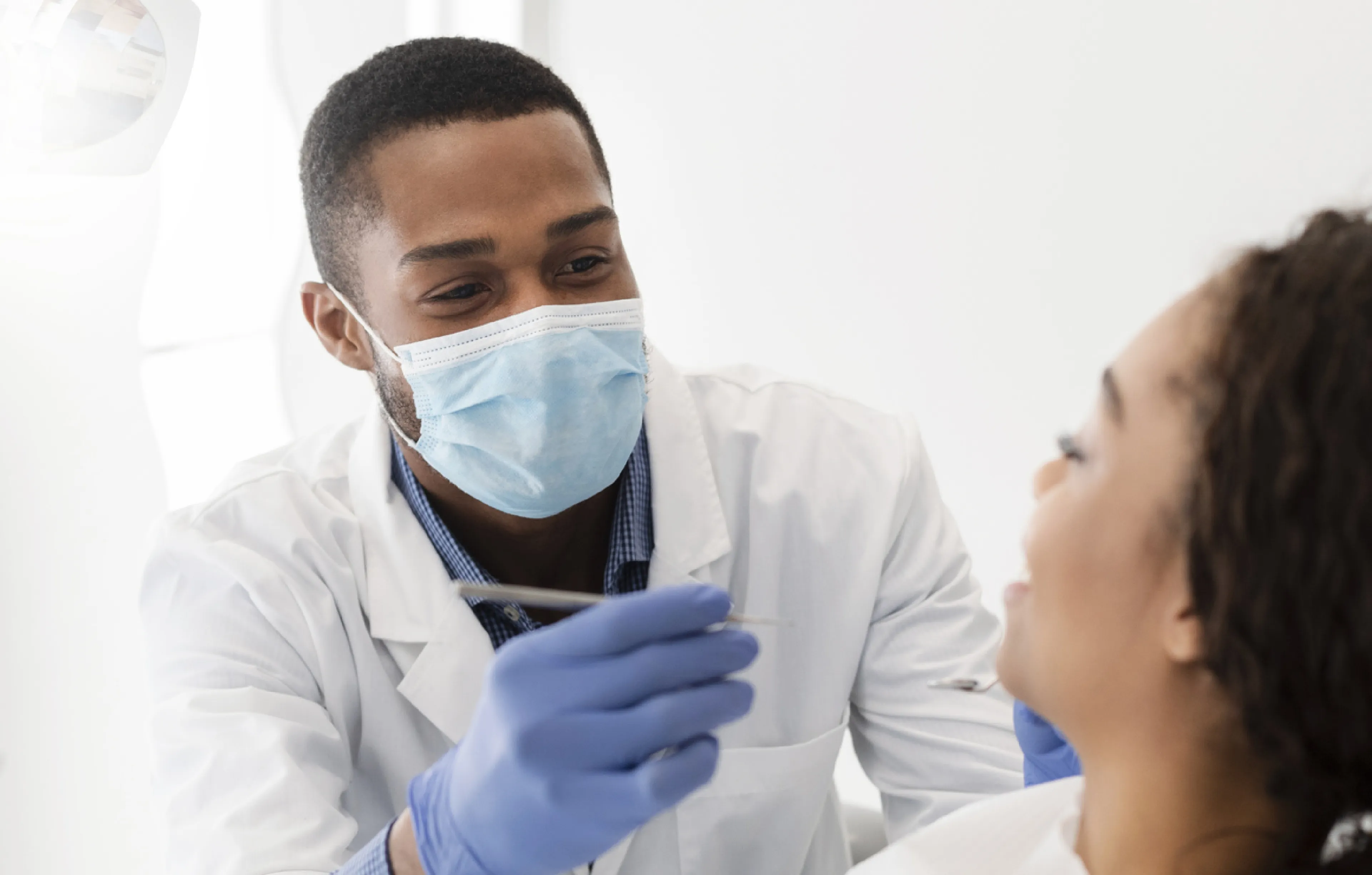 A dentist wearing a mask and gloves focuses on examining a patient seated in a dental chair.